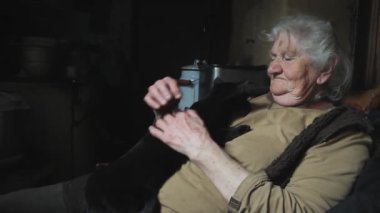 Gri saçlı yaşlı bir kadın siyah kedisini kollarına aldı, onunla oynuyor, gülümsüyor, terk edilmiş bir köyde yaşıyor, seçici odak.