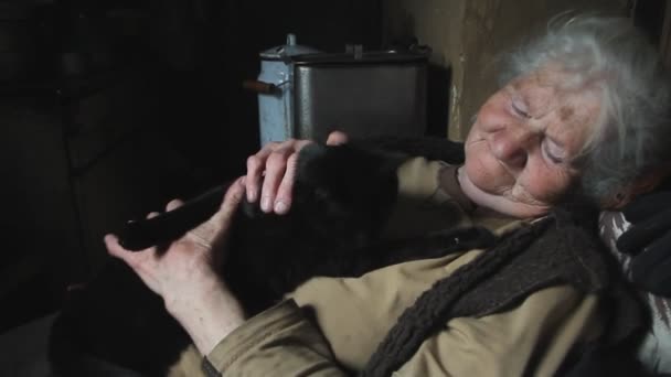 白髪の老婆は 彼女の腕の中に彼女の黒猫を保持し 彼女と遊ぶ 放棄された村に住んで 選択的な焦点 — ストック動画