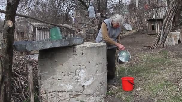 Старуха в заброшенной деревне собирает воду из колодца в ведре, живет одна. — стоковое видео