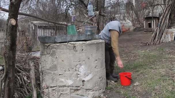 Старуха в заброшенной деревне собирает воду из колодца в ведре, живет одна. — стоковое видео