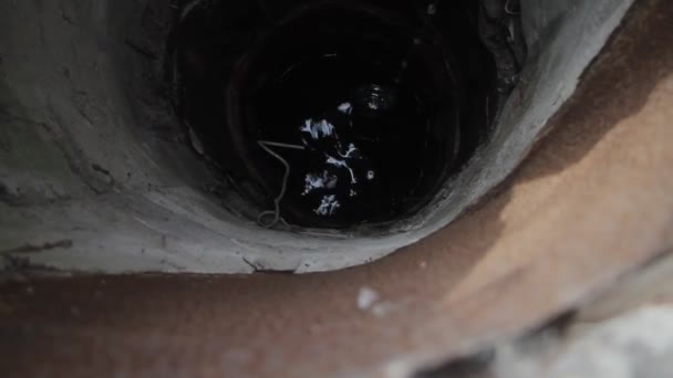 Una anciana en un pueblo desierto está recogiendo agua de un pozo en un cubo, viviendo sola — Vídeo de stock