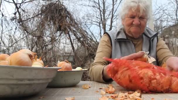 Una anciana con pelo gris recoge cebollas antes de cocinar en la cocina, verduras orgánicas, su propia cosecha — Vídeos de Stock