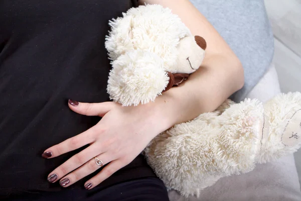 Closeup of the hand of a girl in a black t-shirt holding a beige bear — Stock Photo, Image