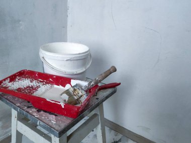 Beyaz boya ve fırçalar ve ışık duvarlar üzerinde bir boya kovası ile kırmızı bir tepsi closeup