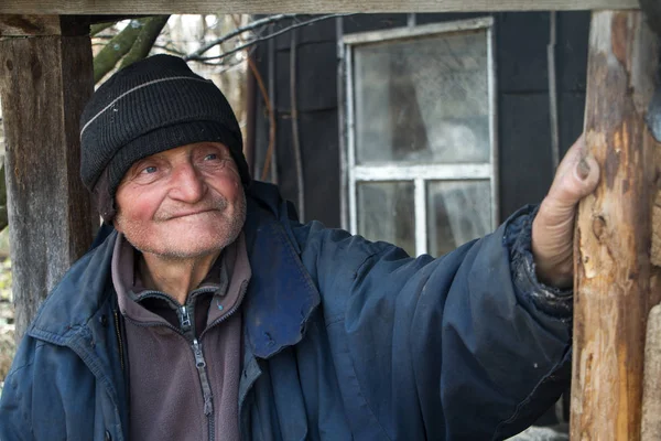一个穿着草率衣服的老人站在自己破房子的门槛上，看着远处 — 图库照片