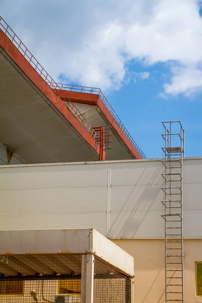 Vista inferior del techo del pabellón industrial, valla y escaleras sobre el cielo azul y las nubes — Foto de Stock