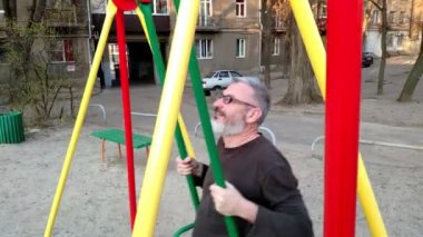 Gri saçlı sakallı adam bir salıncak sürme, sevinir ve gülümsüyor, mutlu bir çocukluk kavramı.