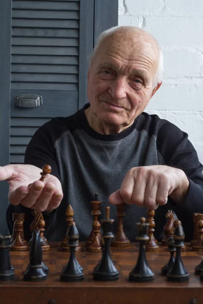 An old man is sitting in front of a chessboard, thinking and making the first move in the game