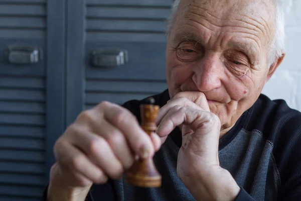 O velho segura em suas mãos a peça de xadrez do rei, o conceito de ganhar ou perder — Fotografia de Stock