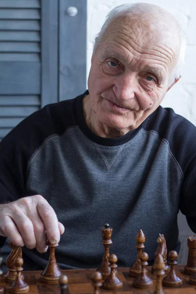 An old man is sitting in front of a chessboard, thinking about the next move in a chess game