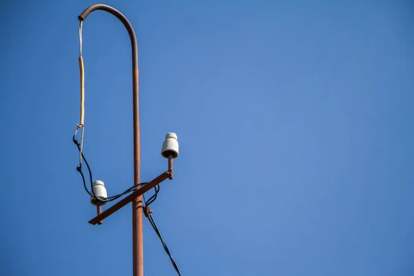 Pólo elétrico velho com isoladores cerâmicos e fios sobre um céu azul, foco seletivo — Fotografia de Stock