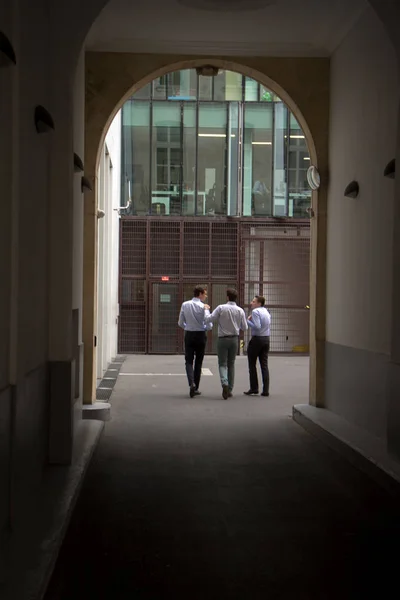 Three male office workers walk down the street through the archway and talk. — Stock Photo, Image