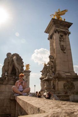 Kız Üçüncü İskender köprüsünde merdivenlerin korkuluk oturur ve akıllı telefon içine bakar