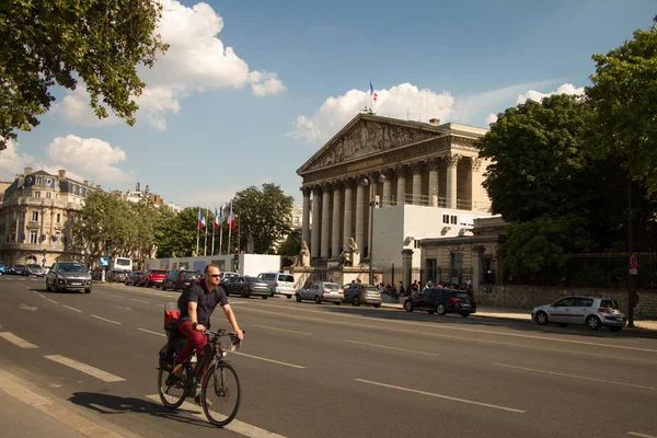 Un hombre monta en bicicleta a lo largo de la carretera a lo largo del Assamley Nacional en París . — Foto de Stock