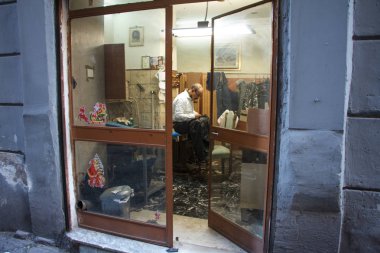 İtalyan terzi Napoli sokakta atölyesinin cam kapı arkasında oturuyor