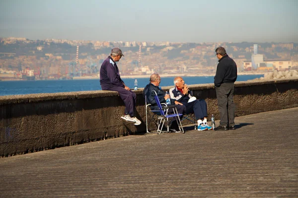 Elderly people sitting on the promenade of Naples are relaxing and talking among themselves against the background of Vesuvius — Stock Photo, Image