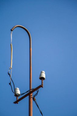 Mavi gökyüzü üzerinde seramik yalıtkanlar ve teller ile eski elektrik direği, seçici odak