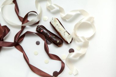 Çikolata damlaları, beyaz ve kahverengi ipek kurdele ile süslenmiş beyaz bir yüzey üzerinde izole farklı dolgular ve tasarım ile iki eclairs bir dizi yakın çekim
