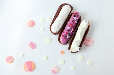 Farklı dolgular ve tasarım beyaz çikolata damlaları ile dekore edilmiş beyaz bir yüzey üzerinde izole ile üç eclairs bir dizi