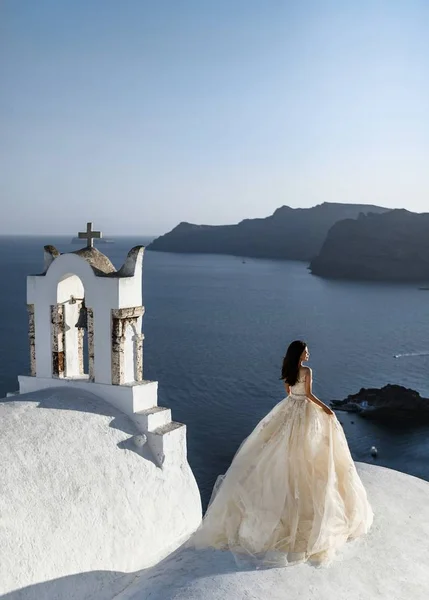 Menyasszony egy szép esküvői terv áll a tetőn a ház, és élvezi a kilátás a tengerre és az ég a nászút Görögországban — Stock Fotó