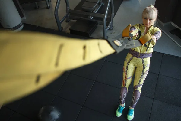 Top view of blonde fitness girl training with trx fitness straps in the gym