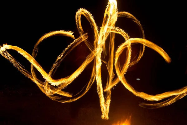De kunstenaar toont een vuurshow 's nachts draaiende toortsen, cirkels van vuur en lussen — Stockfoto