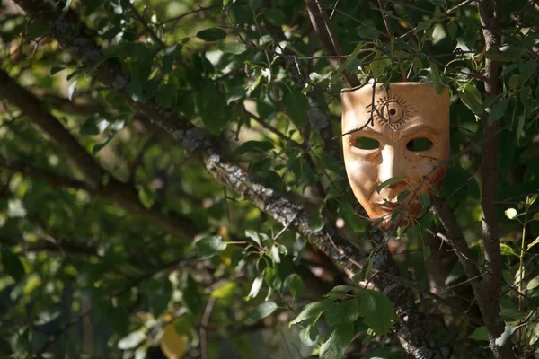 Beige realistische papier-mache masker met zon symbool op voorhoofd opknoping in groene takken van boom — Stockfoto