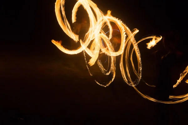 Художник показывает огненное шоу ночью, вращая факелы, круги огня и петли — стоковое фото
