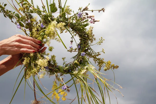 Mani di donna che creano la corona di fiori selvatici su un cielo blu nuvoloso — Foto Stock