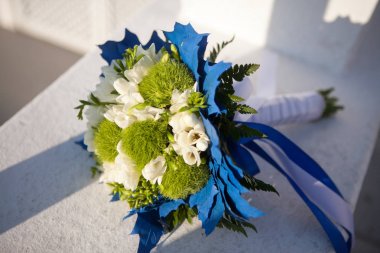 Beyaz ve yeşil renklerde düğün buketi ve beyaz bir yüzey üzerinde mavi dekorasyon