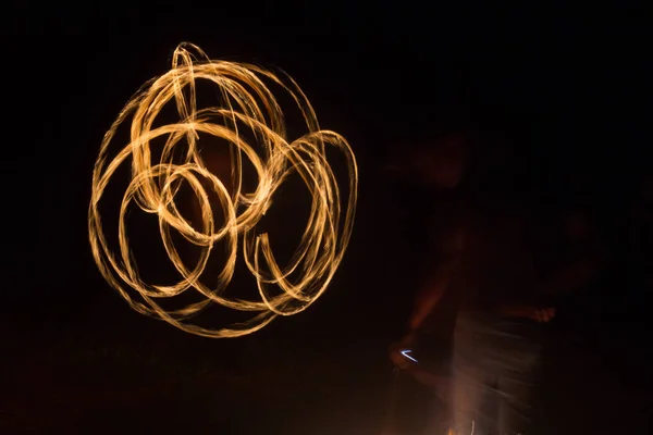Художник показывает огненное шоу ночью, вращая факелы, круги огня и петли — стоковое фото