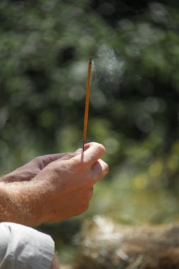 Bulanık doğal arka planda yanan tütsü çubuğu tutan bir adamın eli, seçici odak