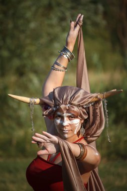 Başında boyalı yüz ve boynuzları ile genç kadın dansçı dans poz duruyor ve kameraya bakıyor