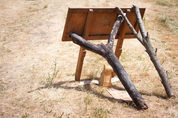 Een houten wegwijzer valt en twee knoige takken ondersteunen het tegen de achtergrond van verdord gras. — Stockfoto