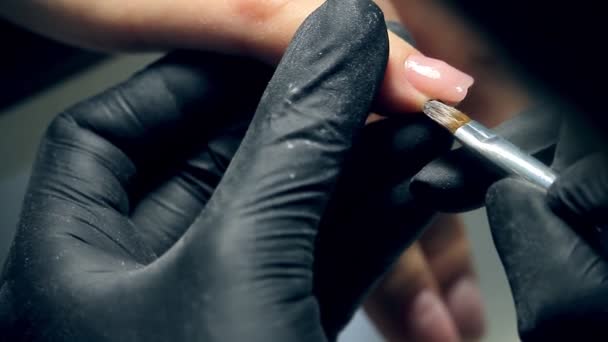 Odborná péče o nehty v procesu, kosmetika v černých rukavicích, která dělá hřebíky pro manikúru s polygelovou krytou