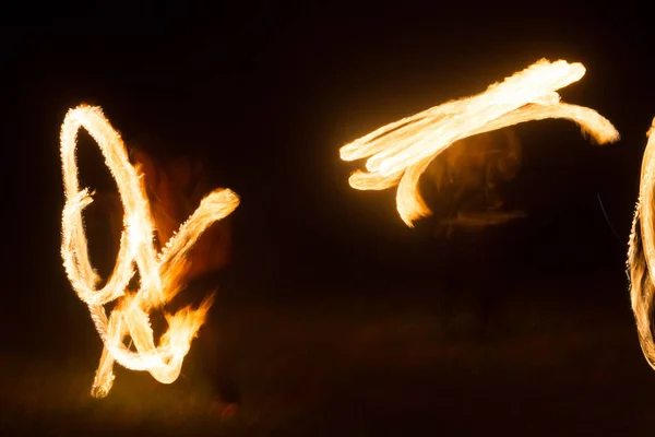 De kunstenaar toont een vuurshow 's nachts draaiende toortsen, cirkels van vuur en lussen — Stockfoto