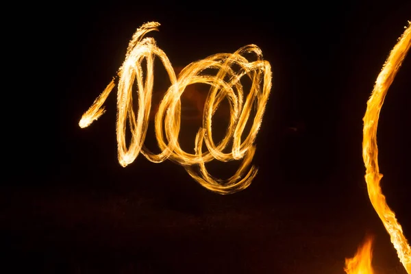 El artista muestra un espectáculo de fuego en la noche girando antorchas, círculos de fuego y bucles — Foto de Stock