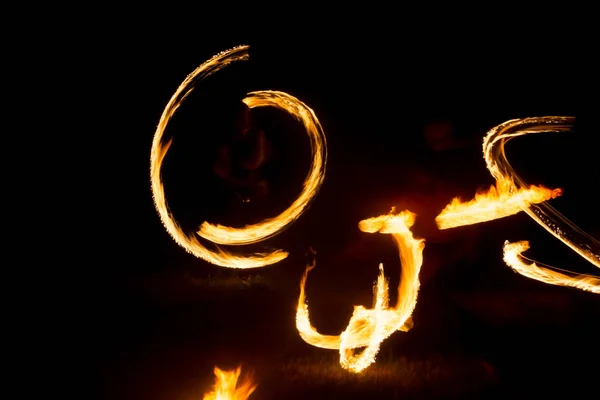 De kunstenaar toont een vuurshow 's nachts draaiende toortsen, cirkels van vuur en lussen — Stockfoto