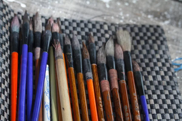 Primo piano di molti pennelli multicolore sdraiati su un tappeto di scacchi e pronti a dipingere, messa a fuoco selettiva — Foto Stock