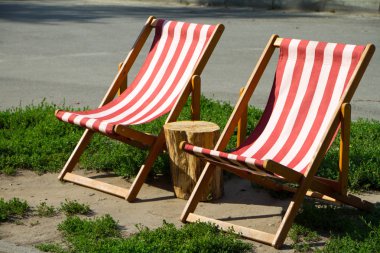 Parktaki iki rahat kırmızı ve beyaz şezlongun ve aralarında bir kütüğün yakın çekim