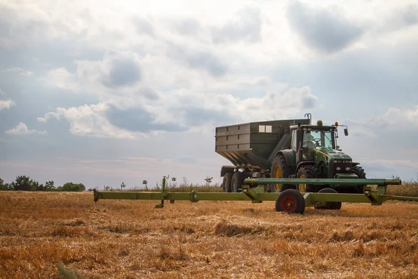 Трактор для збору пшениці з зернозбиральних комбайнів стоїть на полі скошеної пшениці проти блакитного хмарного неба — стокове фото