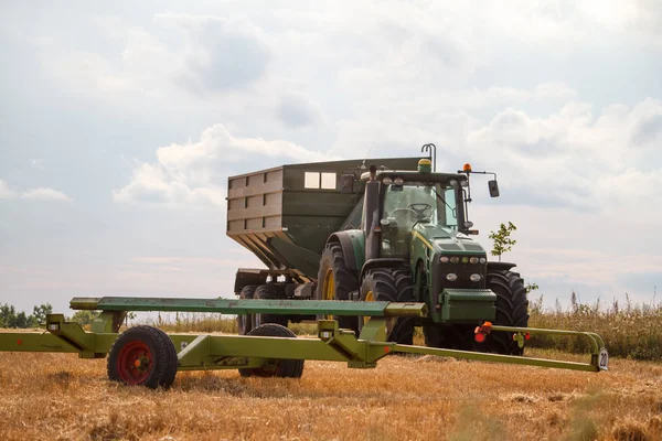 Трактор для збору пшениці з зернозбиральних комбайнів стоїть на полі скошеної пшениці проти блакитного хмарного неба — стокове фото