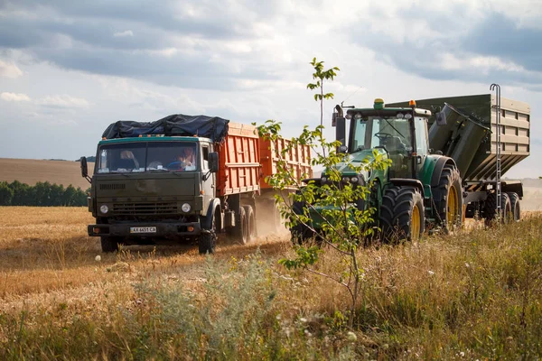 Сільськогосподарська техніка КАМАЗ і трактор стоять пліч-а-пліч на скошеної пшеничному полі під час збору врожаю — стокове фото