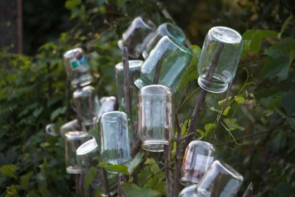 Close-up van verschillende glazen potten worden gedroogd op de kolommen van een houten hek van een wattle hek tegen een groene tuin, selectieve focus — Stockfoto