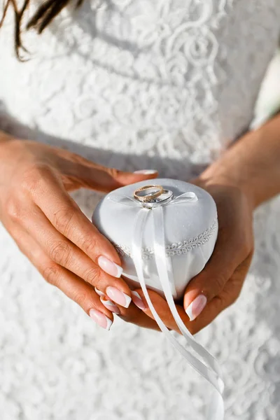 Primer plano de los anillos de boda de oro atados con una cinta de seda blanca a un joyero en las manos de la novia, enfoque selectivo — Foto de Stock