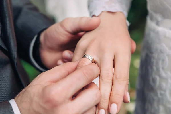 Крупный план руки жениха надевает обручальное кольцо на палец невесты, церемонию на улице, избирательный фокус — стоковое фото