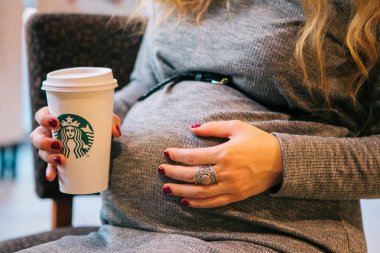 Starbucks, seçici odak bir bardak tutan gri bir elbise hamile bir kadının yakın yukarı göbek