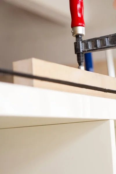 Pegado y fijación de muebles de madera con unas pinzas sobre un fondo borroso de un taller de carpintería, enfoque selectivo —  Fotos de Stock