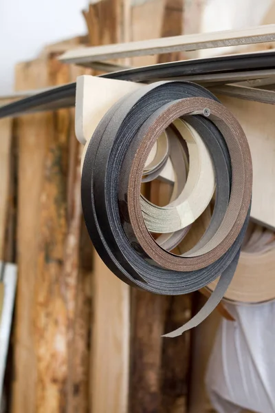 Algunos comenzaron babin borde de PVC y melanina para la fabricación de muebles cuelgan en el estante en un fondo borroso de un taller de carpintería, enfoque selectivo — Foto de Stock