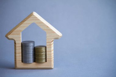 Evin ahşap heykelcik ve gri arka planda içinde sikke iki sütun, satın alma veya bir bina Kiralama kavramı, çevre dostu, seçici odak